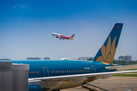 Commercial aircraft taking off with airport apron vehicles and wing view at Tan Son Nhat Airport, Vietnam