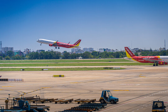 Commercial aircraft taking off with airport apron vehicles and wing view at Tan Son Nhat Airport, Vietnam