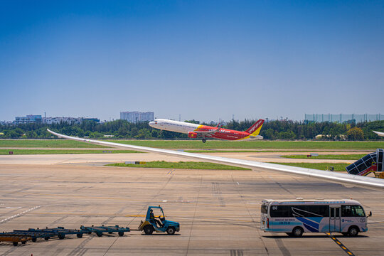 Commercial aircraft taking off with airport apron vehicles and wing view at Tan Son Nhat Airport, Vietnam