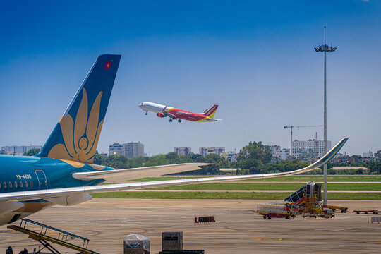 Commercial aircraft taking off with airport apron vehicles and wing view at Tan Son Nhat Airport, Vietnam