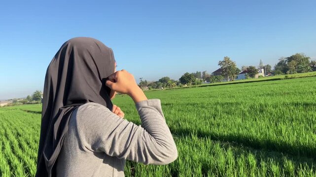 Close-up of a determined young Muslim woman wearing a hijab practicing shadow boxing punches in a beautiful green rice field under a blue sky. Ideal for fitness, self-defense, and empowerment themes.