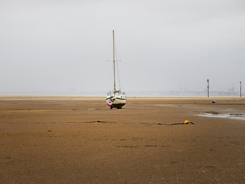 Sailboat stranded on muddy beach at low tide during an overcast