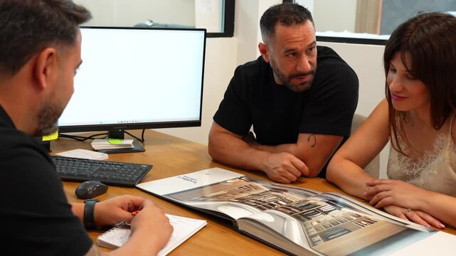 Interior designer consulting a young couple choosing new home furnishings from a catalog