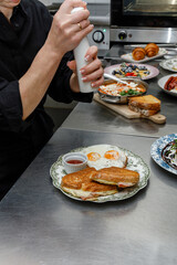 A chef seasons scrambled eggs in the restaurant kitchen. © Cavan