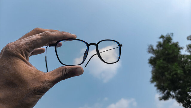Hand Holding Eyeglasses Against Blue Sky Creating Clear Vision Perspective Photography