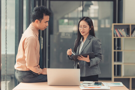 Two Asian business colleagues discussing work project on digital tablet in office.