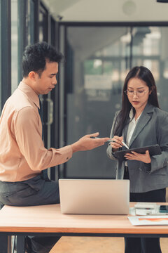 Two Asian business colleagues discussing work project on digital tablet in office.