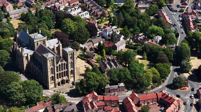 Aerial drone footage of Ripon Cathedral in Ripon North Yorkshire England showcasing the historic medieval cathedral surrounded by mature trees residential streets and the historic city centre