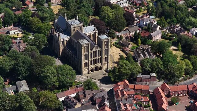 Aerial drone footage circling Ripon Cathedral in Ripon North Yorkshire England highlighting the magnificent medieval cathedral surrounded by mature trees historic streets and residential neighbourhood