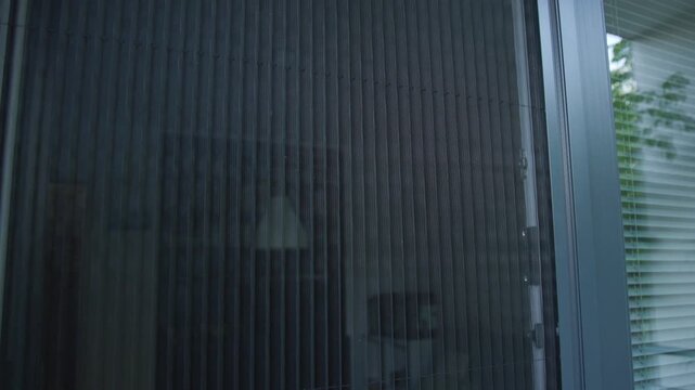 Slow motion of a pleated mosquito net on a window reveals fine vertical mesh folds in cool gray-blue tones, with subtle light passing through in a rhythmic textured pattern.