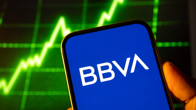 Bbva logo displayed on smartphone screen with digital stock market chart background visual trends.