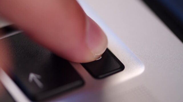 Pressing the power button icon on a silver laptop keyboard. Pushing the on keycap on a computer keyboard extreme close up.