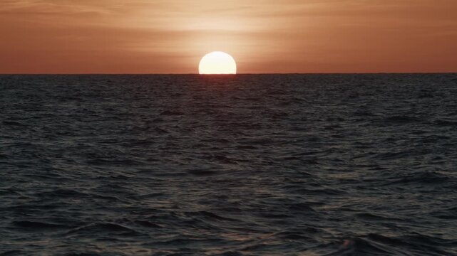 Sunset in the open sea. Sun hides in the sea as seen from the moving sailing vessel.