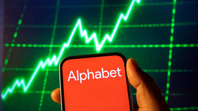 Hand holding smartphone showing Alphabet logo on screen with glowing green stock market chart background.