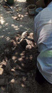 Mason Mixing Sand and Dry Cement with a Shovel on the Ground