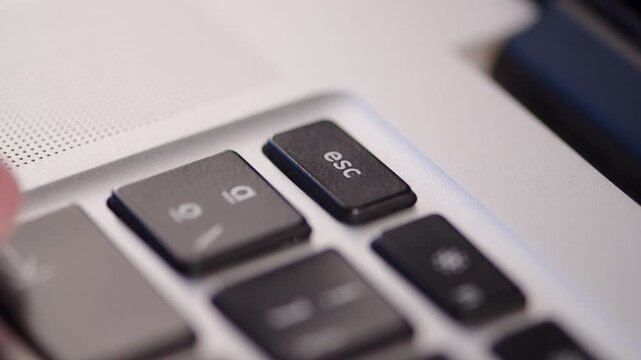 Pressing an escape ESC key on a laptop close up. Canceling a command on a computer. Finger pushing the escape button on a keyboard.