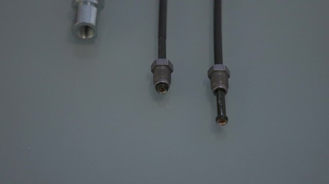 Three automotive brake lines lie on a light gray surface, showing a rubber hose with a threaded fitting on the left and two thin metal brake pipes with flare fittings on the right.