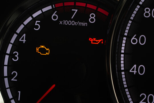 Close-up of car dashboard showing check engine and low oil pressure warning lights on tachometer
