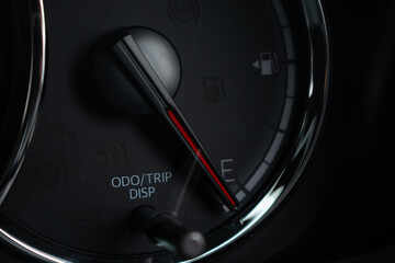 Naklejka premium Close-up of car fuel gauge needle pointing to empty on dark dashboard