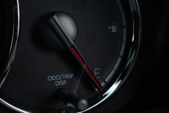 Close-up of car fuel gauge needle pointing to empty on dark dashboard