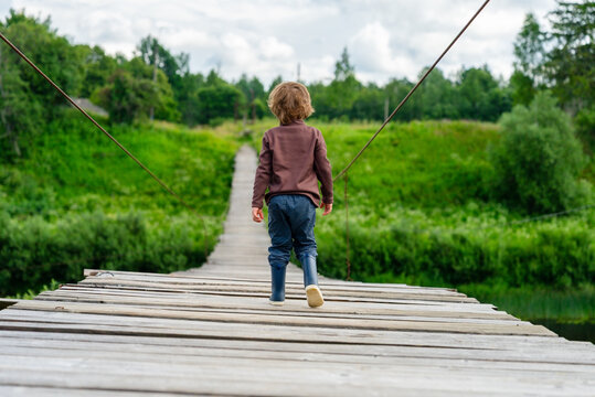 A young child walks across a wooden bridge over green landscape, creating serene and peaceful atmosphere. The little boy explores the scenic rural area with carefree joy.