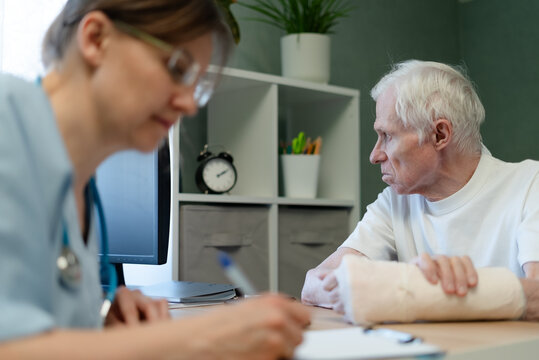 Elderly man reviewing document as nurse explains treatment in clinic. Senior patient engaged while healthcare worker reads chart with helpful focus. Older man learns health literacy at office desk
