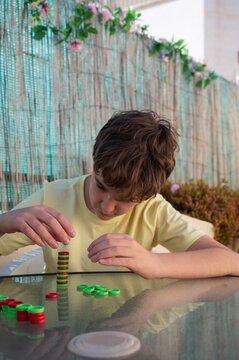 Teenager carefully stacking game pieces while practicing patience and concentration during a strategy game on an outdoor terrace
