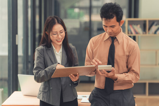 Two Asian business colleagues discussing work project on digital tablet in office.