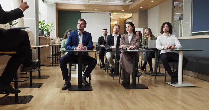 Audience of businesspeople in seminar training presentation. They face the speaker, follow slides, and jot notes while listening closely in a modern venue. Theme: team learning and trust.