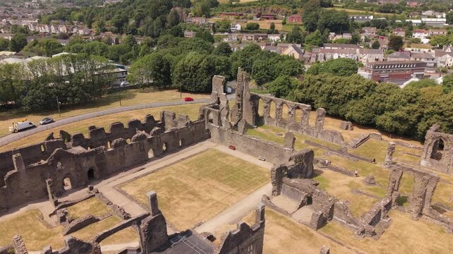 Cinematic drone footage flying above the courtyard of a historic medieval abbey in Wales. Aerial view highlighting Gothic stone arches, ancient monastery ruins, historic architecture and preserved cul