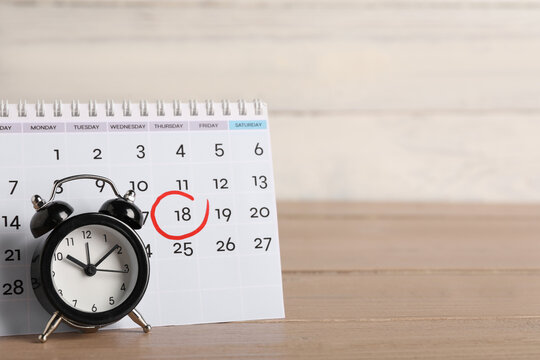 Calendar with marked date and alarm clock on wooden table. Deadline concept