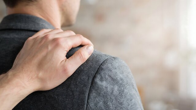Supportive male hand resting on colleague shoulder providing comfort and encouragement during difficult professional situation in modern corporate office setting with soft focus background.