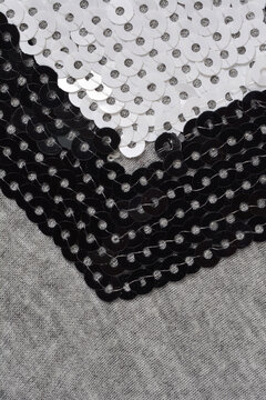 An angled close up shot of a geometric patch made of black and white sequins stitched onto a soft gray melange textile.
