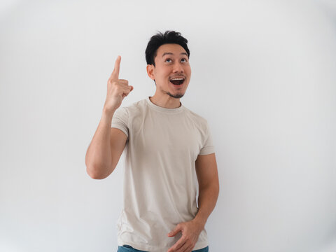 Young Asian man pointing finger up with an excited expression, looking surprised on white background.