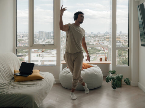 Young Man in Headphones Dancing Freely in His Modern Apartment Living Room with City Views