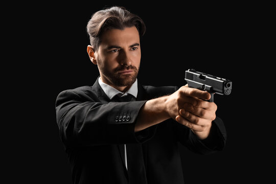 Young male agent with gun aiming on black background