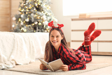 Fototapeta premium Young woman reading book in bedroom on Christmas eve