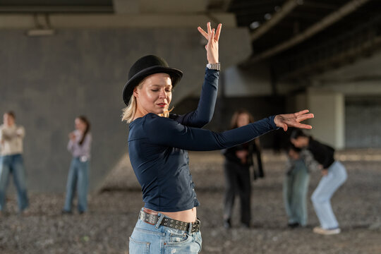 Expressive woman in bowler hat dancing under a bridge