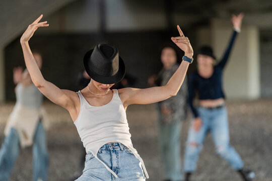 Stylish woman in a fedora dances with her crew