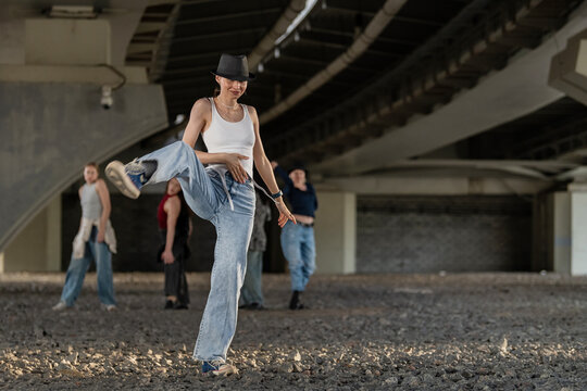 Woman in fedora hat street dancing under a bridge