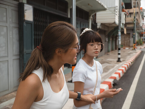 Two Young Asian Women Walking and Talking on a City Street During Daytime