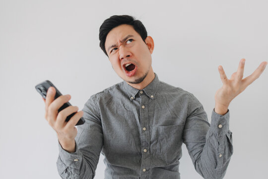 Frustrated Asian Man Holding Smartphone and Gesturing Angrily on White Background