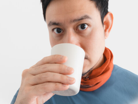 Close-up portrait of an Asian man drinking from a white cup with wide eyes.