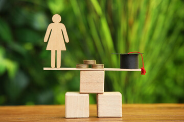 Stand with female figure, coins and graduation hat on table outdoors. Student loan concept