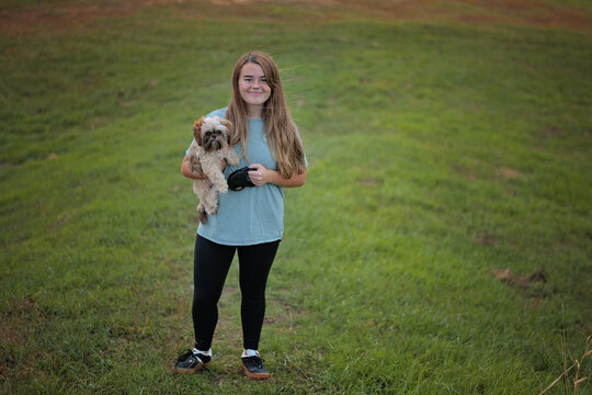 Smiling girl holds fluffy Shih Tzu dog in grassy field