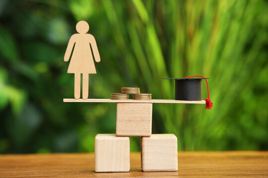 Stand with female figure, coins and graduation hat on table outdoors. Student loan concept
