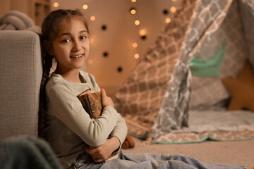 Fototapeta premium Cute girl with adventure book at home in evening