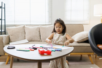 Young asian girl drawing colorful artwork on paper using markers at a coffee table in a modern living room, celebrating childhood creativity and development © David