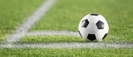 Fototapeta premium Classic black and white soccer ball on a green grass field with white boundary lines, ready for a match