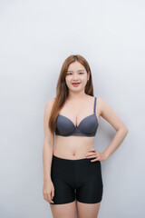 Fototapeta premium Confident Woman in Sportswear: A smiling young woman with long, brown hair stands confidently, wearing a grey sports bra and black athletic shorts.